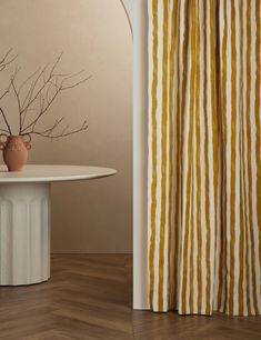 a vase sitting on top of a white table next to a yellow and white curtain