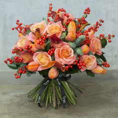 a bouquet of orange roses and berries in a vase on the ground with concrete background