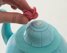 a person is placing a pink bow on top of a blue teapot