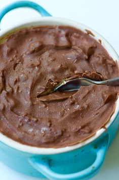 a spoon in a bowl filled with chocolate frosting on top of a blue plate