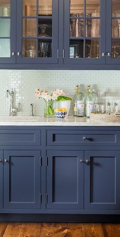 a kitchen with blue cabinets and marble counter tops, white tile backsplash and flowers