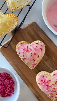 three heart shaped pastries with sprinkles on a cutting board next to two bowls