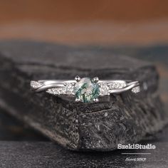 an engagement ring with a green stone surrounded by white diamonds on top of a rock