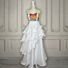 a white dress with multicolored flowers on the bustle and ruffled skirt