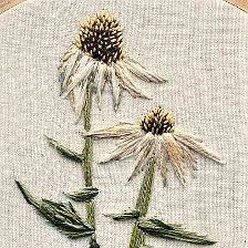 two white flowers with green stems are in the middle of a cross stitched hoop