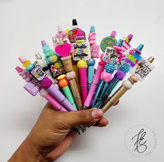 a person's hand holding a bunch of different colored pens and marker pens with writing on them