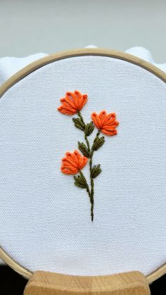 an embroidery project with orange flowers on white fabric and wood frame, sitting on top of a table