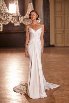 a woman in a white wedding dress standing on a floor with chandelier behind her