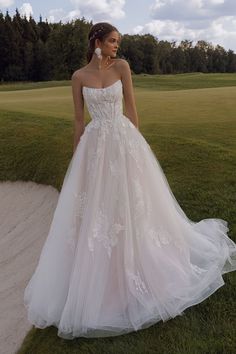 a woman in a wedding dress is standing on the grass near a golf course and trees