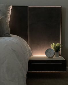 a clock sitting on top of a night stand next to a bed with white sheets