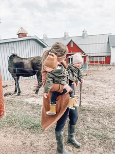 a woman holding a child while standing next to a horse