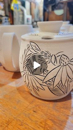 two white cups with designs on them sitting on a wooden counter top next to each other