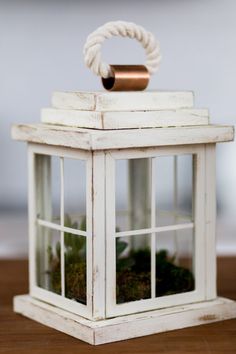 a white lantern with moss inside on a wooden table