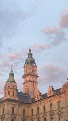 an old building with two towers and a clock on it's side at sunset