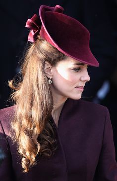 a woman with long hair wearing a red hat and purple coat, looking off to the side