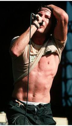 a shirtless man with no shirt on holding his hands up to his head while standing in front of a microphone