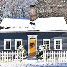 a blue house with white picket fence and wreath on the front door is covered in snow