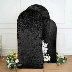 two black velvet tombstones with flowers on the floor in front of white wall and wood flooring