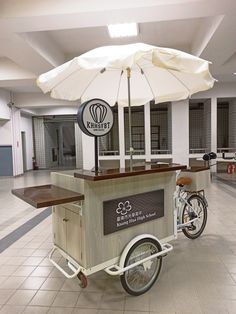 an ice cream cart in the middle of a large room with tables and umbrellas