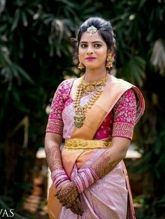 a woman in a pink and yellow sari with gold jewelry on her neck, standing outside