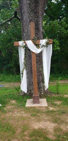 a wooden cross sitting next to a tree with white drapes on it's sides