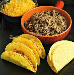 some tacos and other food items are on a black table with orange bowls, spoons and utensils