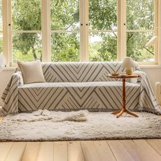 a living room with two windows and a couch in front of the window is covered by a striped cover