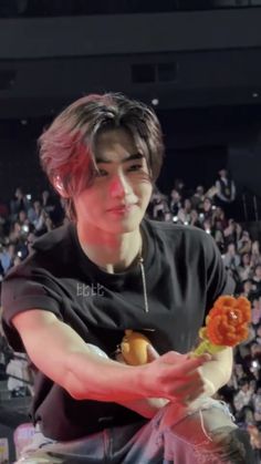 a young man sitting in front of a crowd holding a hot dog and an orange flower