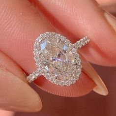 a woman's hand holding an oval shaped diamond ring with diamonds on the band