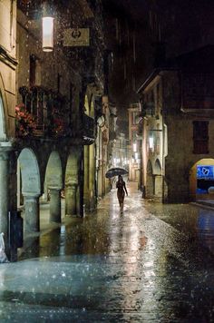 a person with an umbrella walking down the street in the rain on a rainy night