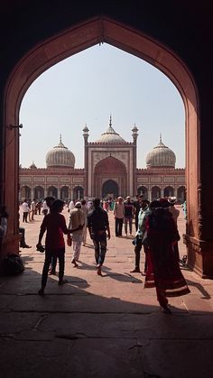 many people are walking around in front of a large building with arches and domes on it