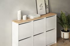 a white cabinet sitting next to a potted plant on top of a hard wood floor