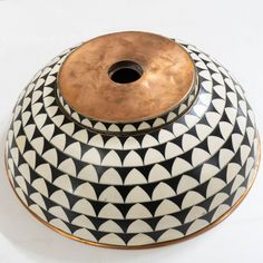 a black and white vase sitting on top of a table next to a brown lid