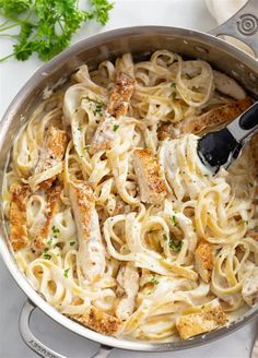 a skillet filled with chicken and pasta on top of a white counter next to parsley