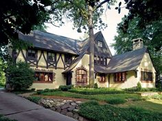 a large house sitting on top of a lush green field next to a forest filled with trees