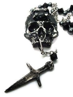 Made to Order! A universal memento mori for your dark wardrobe, this skull pendant is complete with a small dagger to enhance its grim aura. An imposing complement to your most dramatic looks, the pendant is cast in lead free pewter by hand and weathered, then set with a glass or stone cabochon. The chain is accented with hand beaded elements for a finishing touch. It can be layered with one of my rosary chains, or shorter pieces like chokers! Its also perfect on its own with all kinds of outfit choices as a centerpiece. Available in multiple variants Necklace chain default length: 18 in If you'd like a different chain length, please leave a note with your order Time to make and ship: 1-2 days. Gothic Metal Skull Necklace, Black Skull Necklace In Edgy Style, Black Edgy Skull Necklace, Medieval Black Metal Necklace, Medieval Style Black Metal Necklace, Black Gothic Necklaces For Larp, Gothic Hand-cast Skull Jewelry, Black Skull Necklace With Oxidized Finish, Black Oxidized Skull Necklace