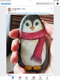 a hand holding a rock with a penguin painted on it and a scarf around its neck