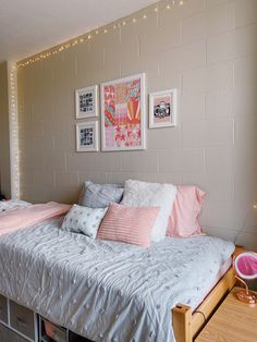 there is a bed with pink and white pillows in the room that has pictures on the wall above it