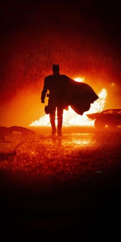 the silhouette of a man in a caped suit walking through a fire with a car behind him