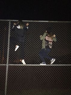 two people jumping on a fence at night