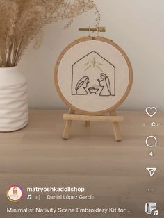 a cross stitch nativity scene is displayed in front of a vase with dried grass