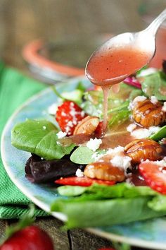 someone pouring dressing onto a salad on a plate with spinach leaves and strawberries