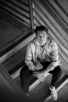 black and white photo of a man sitting on stairs with his hands in his pockets