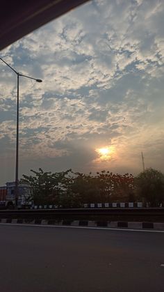 the sun is setting behind some clouds in the sky over a street with cars on it