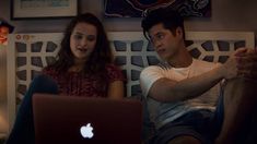 a man and woman sitting on a bed with an apple laptop computer in front of them