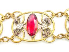 "This lovely bracelet features oval bezel set rhinestones in a deep ruby red color. The stones are flanked by white enamel flowers with red leaves that coordinate with the stones. These stones and enamel are all set in antique brass links. This wide, delicate bracelet has all the hallmarks of a Neiger piece (although these were not signed, so it's a bit hard to be sure). In any event, this is a prime example of Art Deco Czech jewelry. CONDITION/SIZE: Excellent vintage condition. About 7.5\" long Red Oval Art Deco Jewelry, Vintage Red Gemstone Bracelets, Ruby Red Color, Czech Jewelry, Red Leaves, Deco Jewelry, Enamel Flower, Red Rhinestone, Rhinestone Bracelet