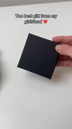 a hand holding a piece of black paper next to a mouse on a white surface