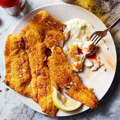 a white plate topped with fried fish next to lemon wedges and mashed potatoes