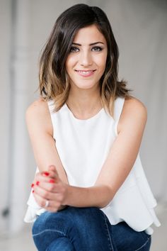 a woman sitting on the ground with her arms crossed and smiling at the camera while wearing a white top