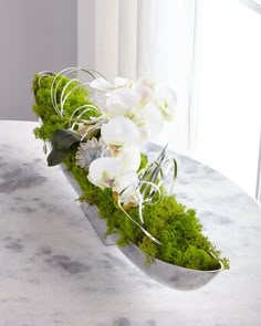 an arrangement of white flowers and greenery on a marble countertop in front of a window